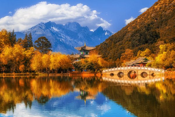 Paisaje de Yunnan, es un gran lago con un puente y árboles, montañas con nubes de fondo.