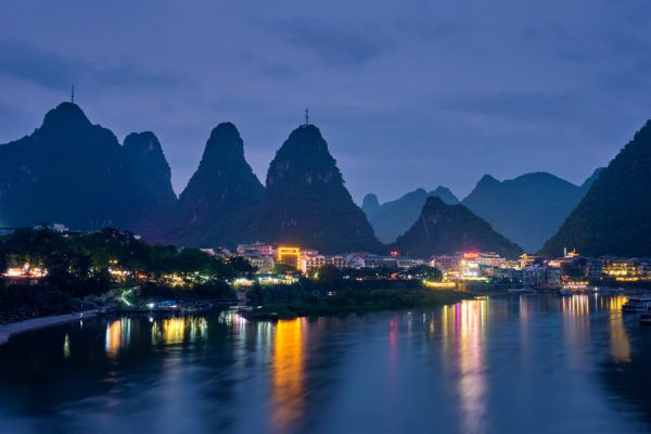 Fotografía de noche de la ciudad de Yangshuo donde se aprecia el lago y la ciudad iluminada con sus altas montañas.